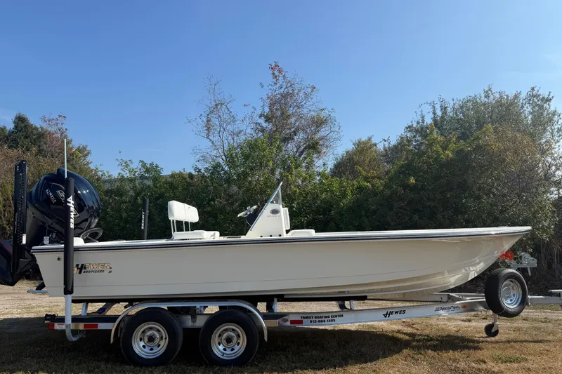 Slide: The Image of 2026 Hewes 21 REDFISHER boat on trailer, parked outdoors with trees in background. - 8