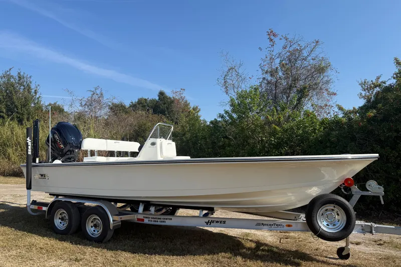 Slide: The Image of 2026 Hewes 21 REDFISHER boat on trailer, parked outdoors under clear blue sky. - 9