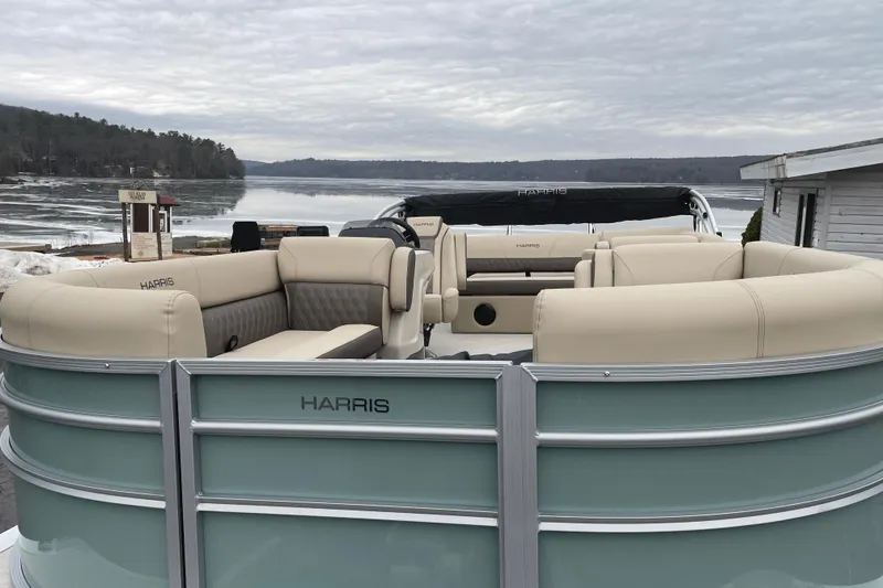 Slide: The Image of 2026 Harris Cruiser 230 pontoon boat with beige seating, docked by a serene lake. - 4