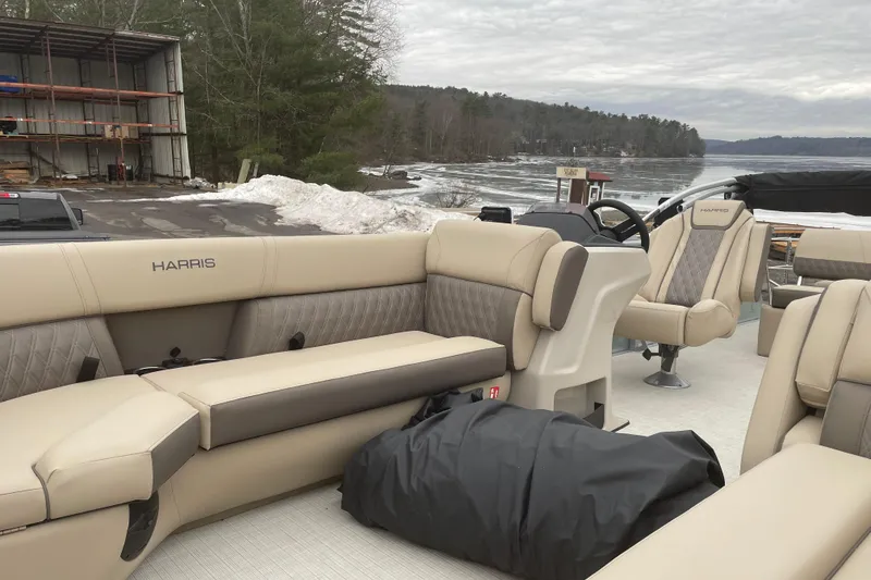 Slide: The Image of 2026 Harris Cruiser 230 pontoon boat interior with beige seating, docked by a snowy lakeside. - 5