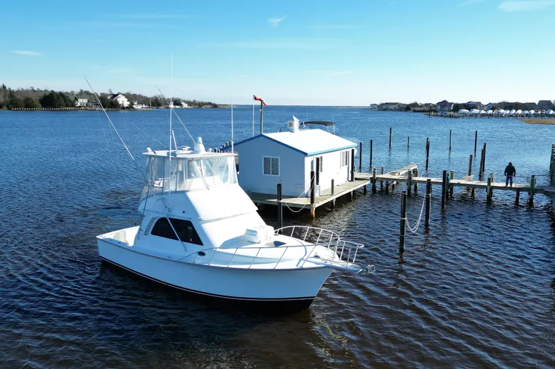 The Image of 2003 Henriques Yachts 35 Sportfisherman cruising on a serene lake with waterfront homes. - 0
