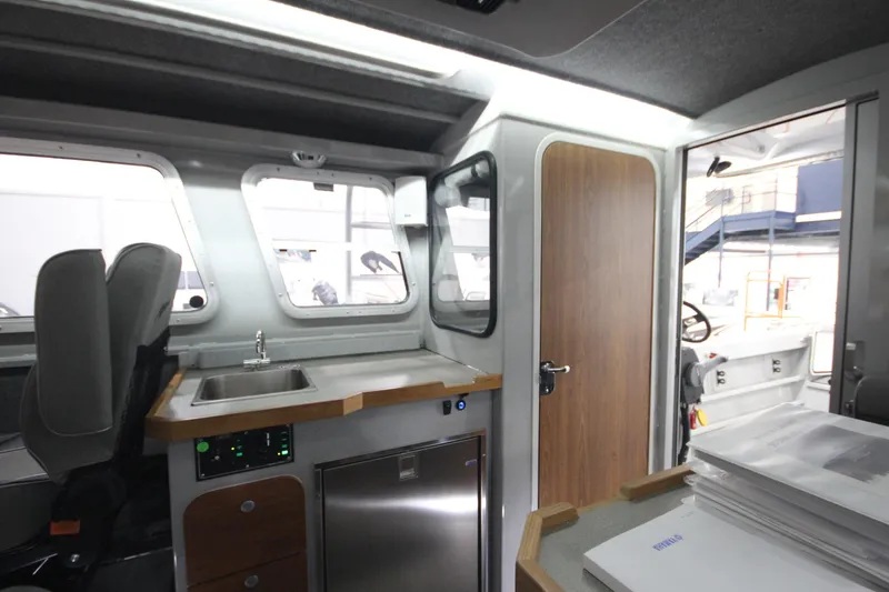 Slide: The Image of Interior of 2025 Weldcraft 300 Cuddy King OS, featuring kitchenette and seating area. - 23