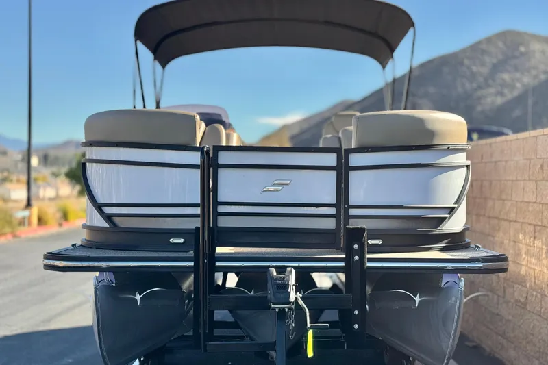 Slide: The Image of 2021 Starcraft SLS 3 pontoon boat with canopy, parked on a trailer, mountain backdrop. - 2