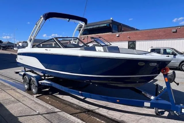 The Image of 2025 Cobalt CS23 Surf boat on trailer, blue and white design, parked outdoors. - 0