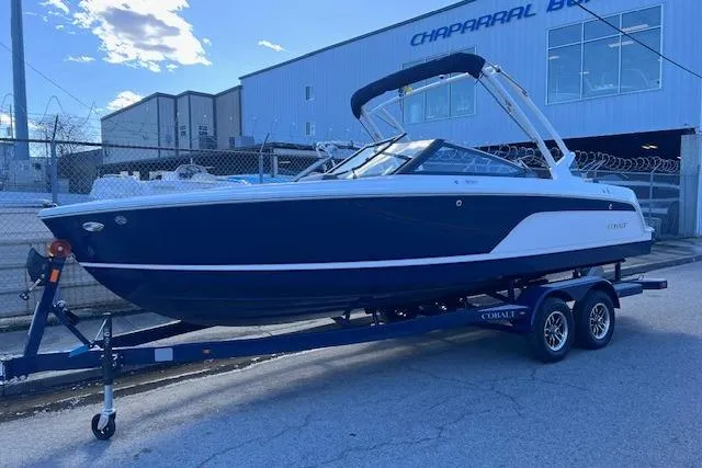 Slide: The Image of 2025 Cobalt CS23 Surf boat on trailer, parked outdoors near industrial building. - 3