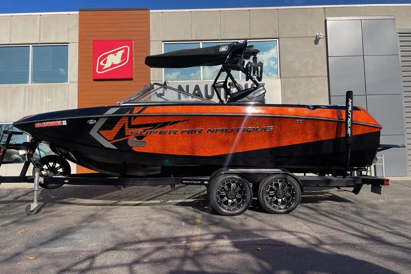 The Image of 2015 Nautique Super Air Nautique G23 boat in vibrant orange and black, parked on a trailer. - 1