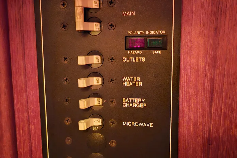 Slide: The Image of Electrical panel with switches for outlets, water heater, battery charger, and microwave in a 1994 Tartan 3100. - 14