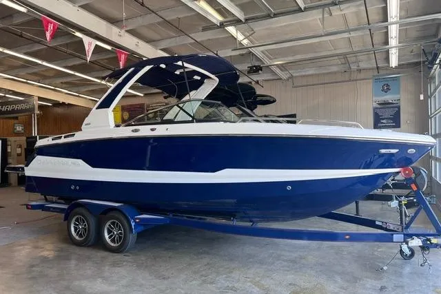 The Image of 2025 Chaparral 267 SSX boat in showroom, blue and white design on trailer. - 0