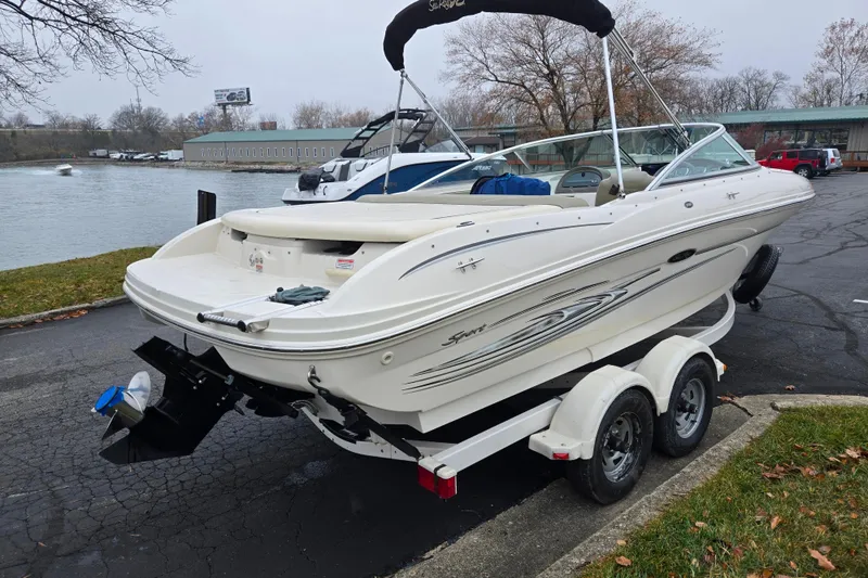 Slide: The Image of 2004 Sea Ray 200 Sport boat on trailer by a riverside parking area. - 1