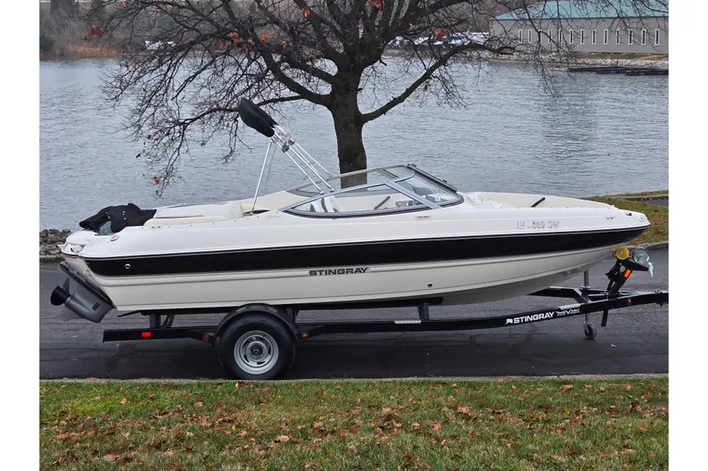 The Image of 2016 Stingray 198 RX boat on trailer by a lake, overcast day. - 0