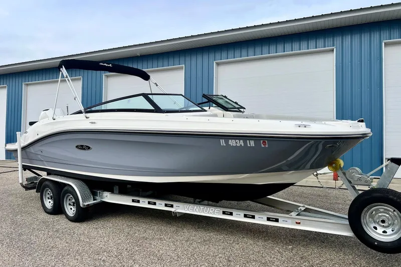 Slide: The Image of 2023 Searay SPX230 boat on trailer, parked outside blue warehouse. - 2