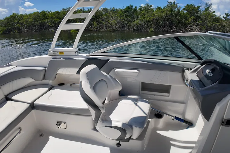 Slide: The Image of 2020 Chaparral 23 SSi boat interior with seating and steering, near lush shoreline. - 18