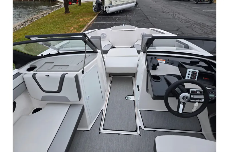 Slide: The Image of 2025 Yamaha Boats AR220 interior with modern dashboard and seating, docked near a grassy area. - 11