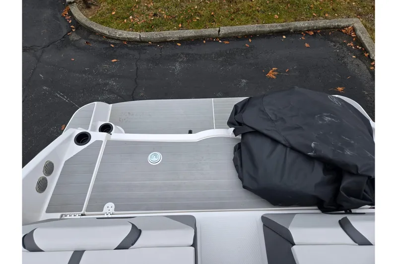 Slide: The Image of 2025 Yamaha Boats AR220 deck with seating and cover, parked on asphalt. - 27