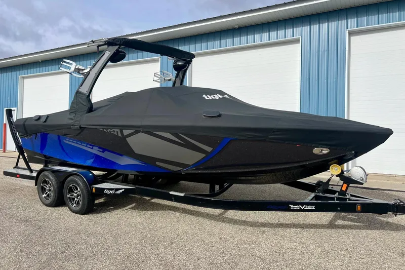 Slide: The Image of 2017 Tigé R21 boat with cover on trailer, parked outside blue building. - 3