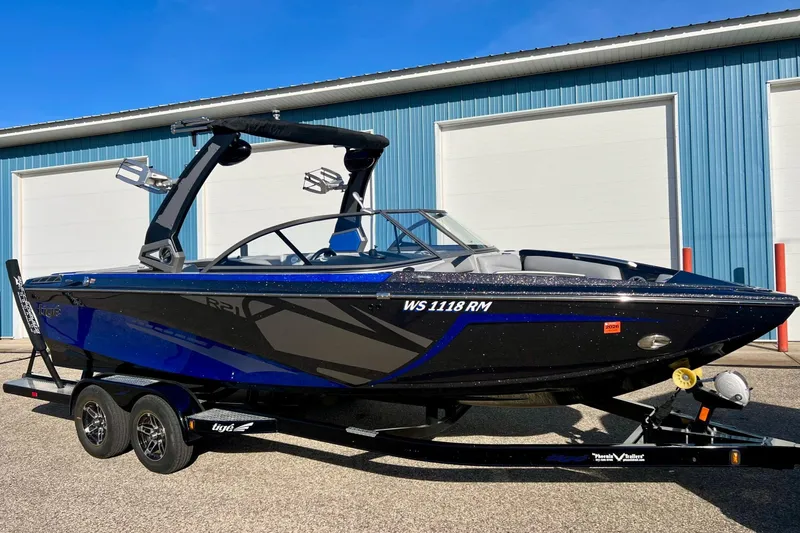 Slide: The Image of 2017 Tigé R21 boat in blue and black, parked on a trailer outside a blue building. - 6