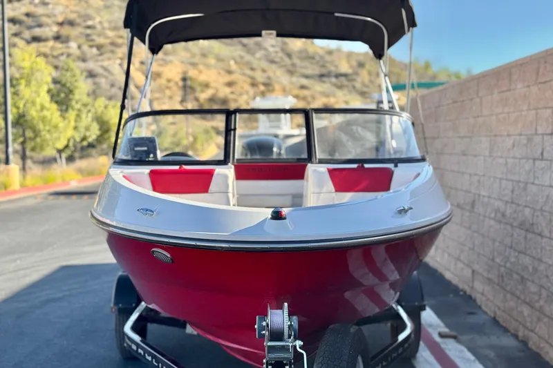 Slide: The Image of 2016 Bayliner 180 Bowrider boat with red hull, parked on a trailer. - 2