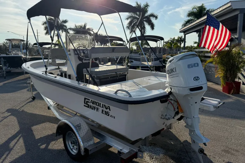 Slide: The Image of 2026 Carolina Skiff E16 JVX CC boat with Suzuki 60 engine, parked near American flag. - 10