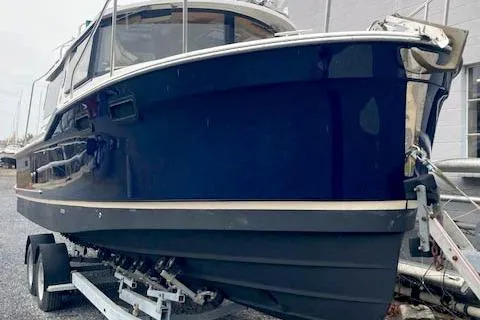 The Image of 2018 Ranger Tugs R-27 boat on trailer, navy blue hull, docked outdoors. - 0