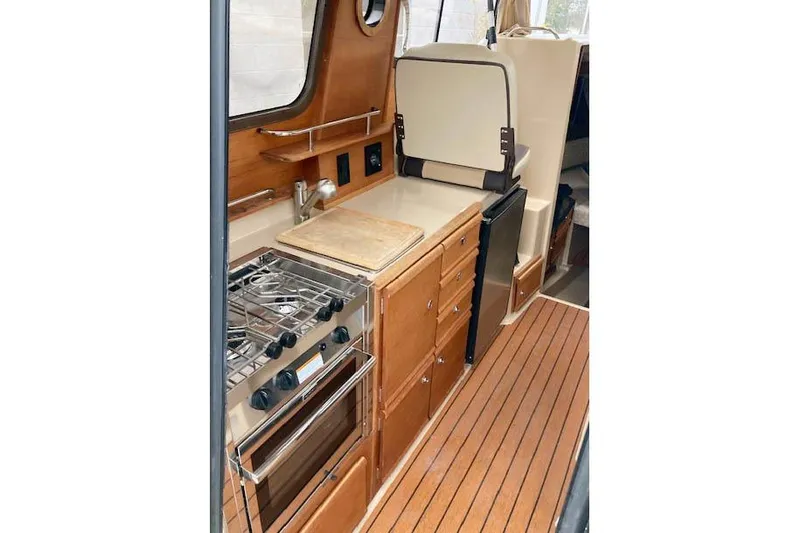 Slide: The Image of 2018 Ranger Tugs R-27 interior kitchen with stove, wooden cabinetry, and compact design. - 18