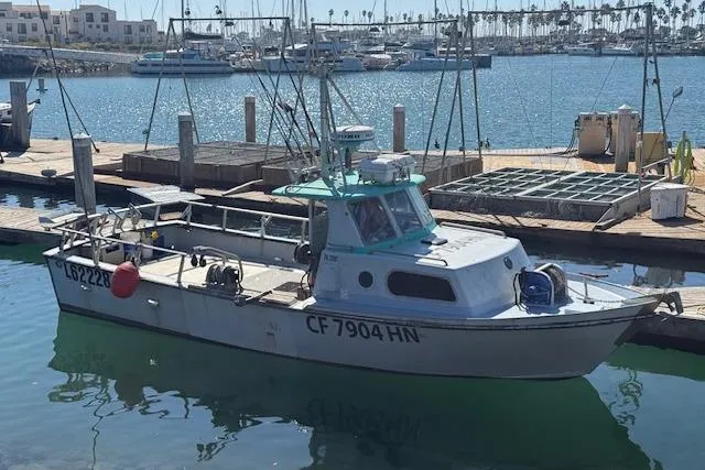 The Image of 1982 Willard Vega 30 boat docked at a marina, with clear blue water and other boats in the background. - 0
