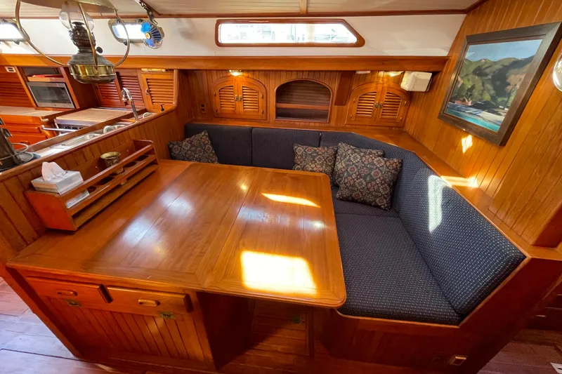 Slide: The Image of Cozy 1985 Passport 40 yacht interior with wooden dining area and blue cushioned seating. - 21