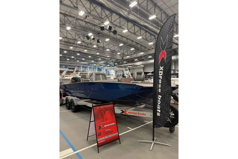 Slide: The Image of 2025 Xpress X23B Bay Lounge boat displayed indoors with promotional signage. - 9