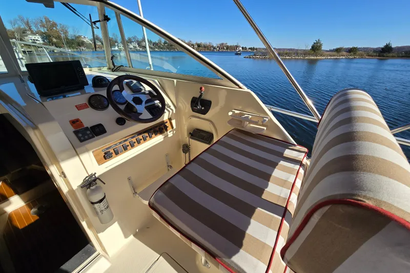 Slide: The Image of 2001 Mainship 30 Pilot Rum Runner cockpit with striped seating, steering wheel, and water view. - 3