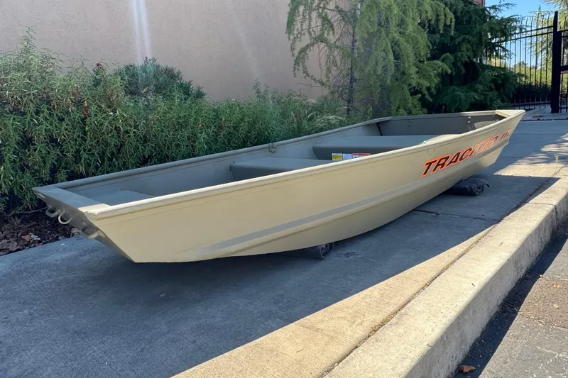 Slide: The Image of 2026 Tracker Grizzly 10 Jon boat on pavement, surrounded by greenery. - 2