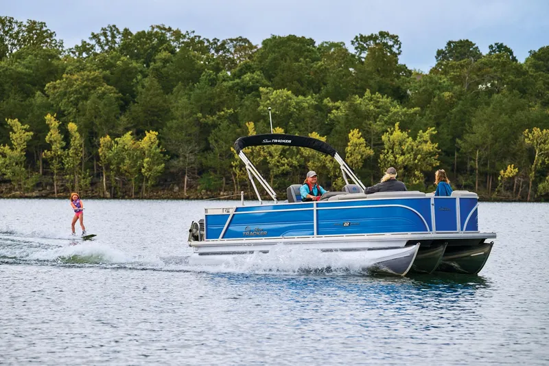 Slide: The Image of 2026 Sun Tracker Party Barge 22 RF XP3 pontoon boat on trailer, parked near blue building. - 2