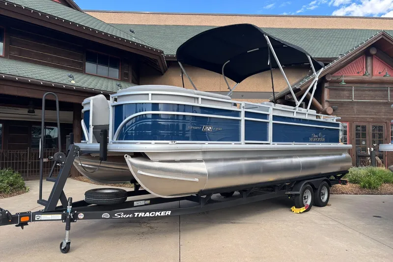 The Image of 2026 Sun Tracker SportFish 22 DLX pontoon boat on trailer, parked outside a building. - 0