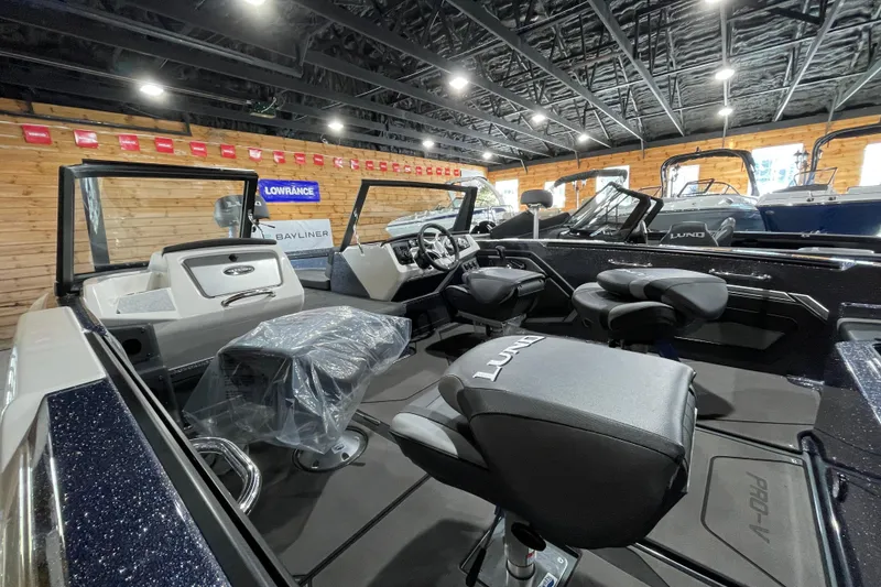 Slide: The Image of 2026 Lund 202 Pro-V GL boat interior with modern seating and dashboard in showroom. - 13