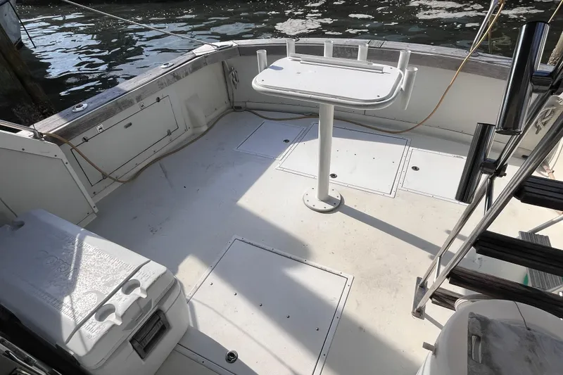 Slide: The Image of 1981 Bertram 35 Sportfish boat deck with fishing table and cooler, docked by the water. - 19