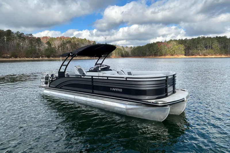 Slide: The Image of 2021 Harris Solstice 250 pontoon boat on a serene lake with forested shoreline. - 11