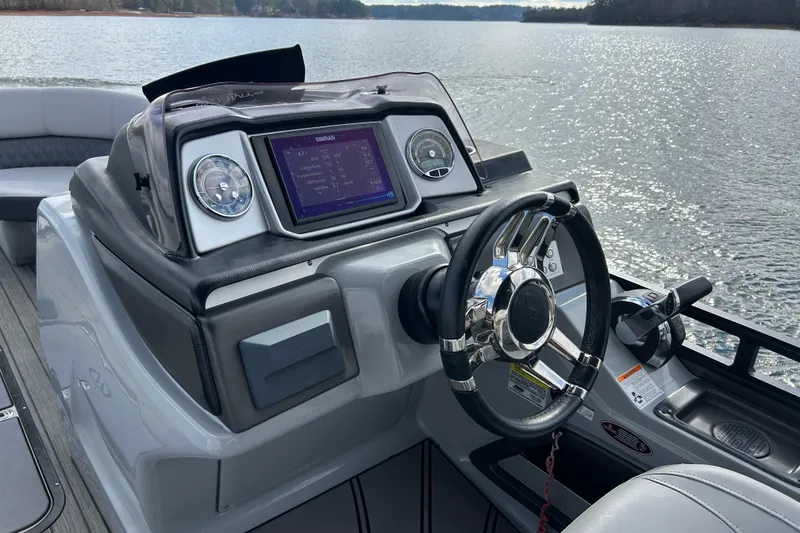 Slide: The Image of 2021 Harris Solstice 250 boat dashboard with steering wheel and digital display on a lake. - 13