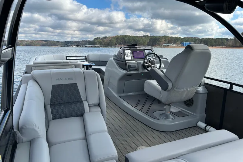 Slide: The Image of 2021 Harris Solstice 250 pontoon boat interior with luxurious seating and helm on a scenic lake. - 21