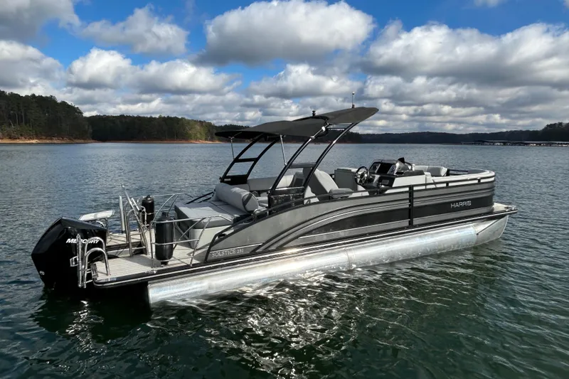 Slide: The Image of 2021 Harris Solstice 250 pontoon boat on a serene lake under a partly cloudy sky. - 8