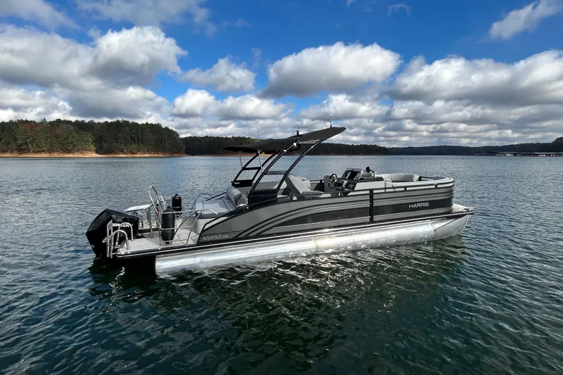 Slide: The Image of 2021 Harris Solstice 250 pontoon boat on a serene lake under a partly cloudy sky. - 9