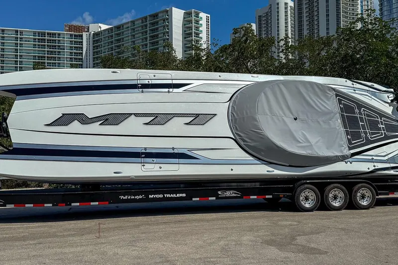 The Image of 2024 MTI 440X boat on trailer, urban backdrop, clear sky. - 0
