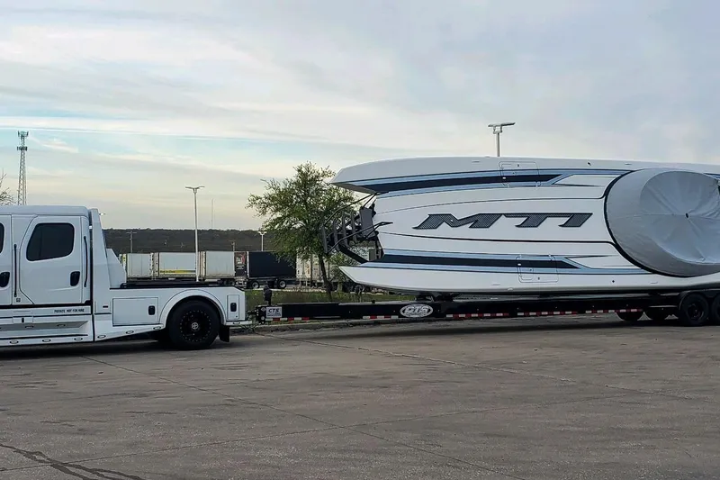 Slide: The Image of 2024 MTI 440X boat on trailer, towed by a white truck in a parking lot. - 6