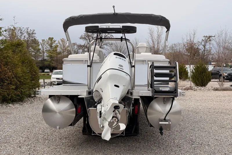 Slide: The Image of 2026 Tahoe Pontoon LTZ Quad Lounger with outboard motor, parked on gravel. - 5