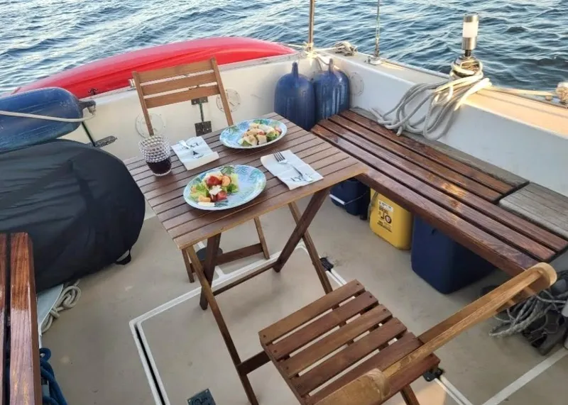 Slide: The Image of 1986 Cape Dory MS300 sailboat deck with dining setup, featuring wooden chairs and table, ocean view. - 15