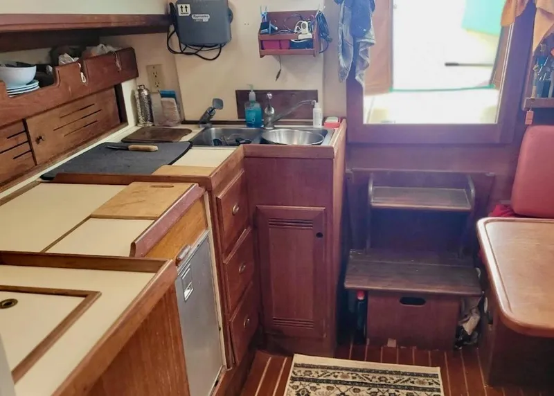 Slide: The Image of 1986 Cape Dory MS300 yacht interior with compact kitchen, wooden cabinetry, and seating area. - 35
