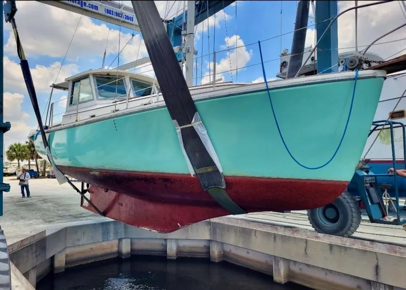 Slide: The Image of 1986 Cape Dory MS300 boat in dry dock, turquoise hull, red bottom, being lifted by crane. - 6