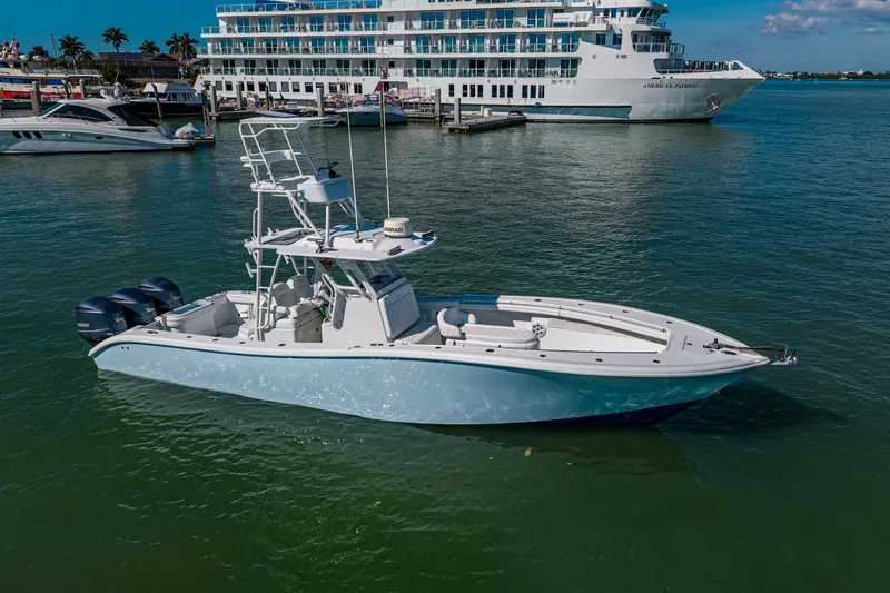 Slide: The Image of 2018 Yellowfin 36 Offshore boat docked, featuring triple outboard engines, with a large ship in the background. - 9