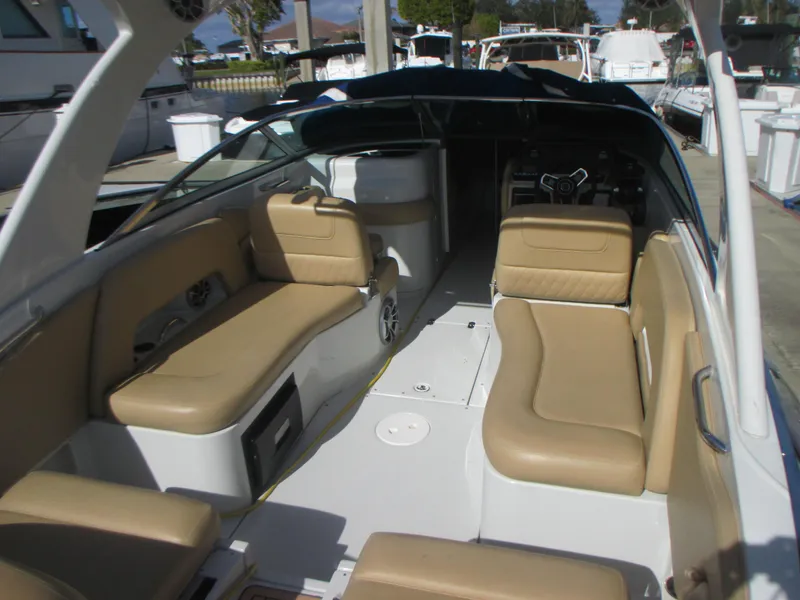 Slide: The Image of 2018 Crownline Eclipse E29 XS boat interior with beige seating and wood flooring at a marina. - 10