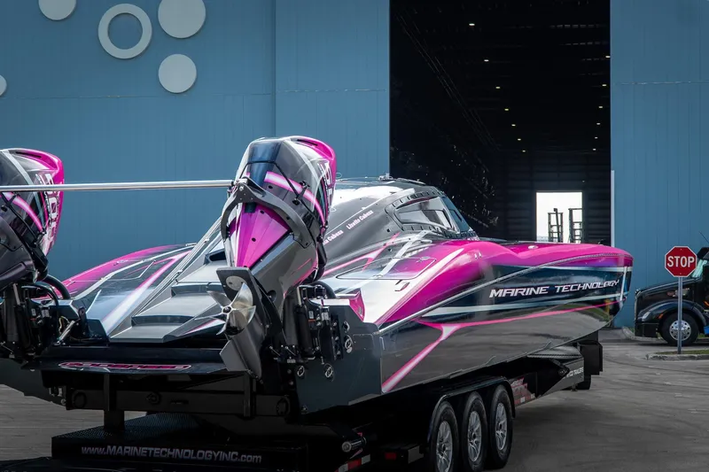 Slide: The Image of 2023 MTI 390XR powerboat with vibrant pink accents, parked outside a large blue building. - 39