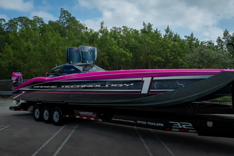 Slide: The Image of 2023 MTI 390XR powerboat on trailer, vibrant pink and black design, parked near trees. - 55