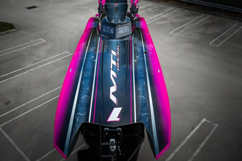 Slide: The Image of 2023 MTI 390XR boat with vibrant pink and blue design in a parking lot. - 57