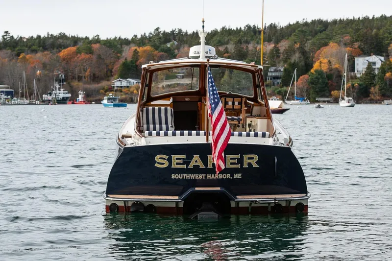 Slide: The Image of Hinckley Picnic Boat Classic 2001 on water, displaying American flag, autumn trees in background. - 13